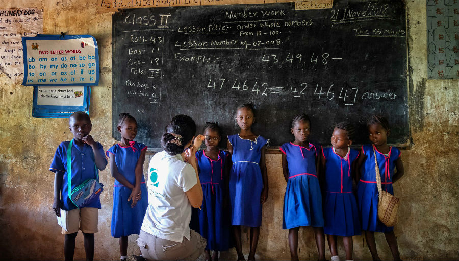 Member stories, lady holding glasses up to a child in africa in a school classroom