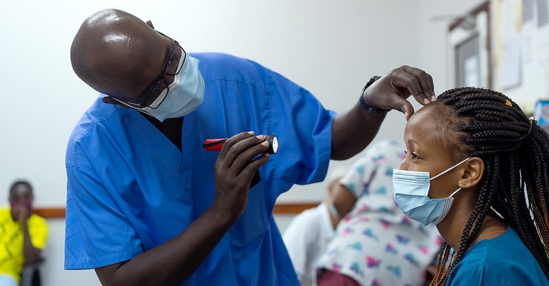 Doctor screening a patient in a clinic with a torch, both wearing face masks