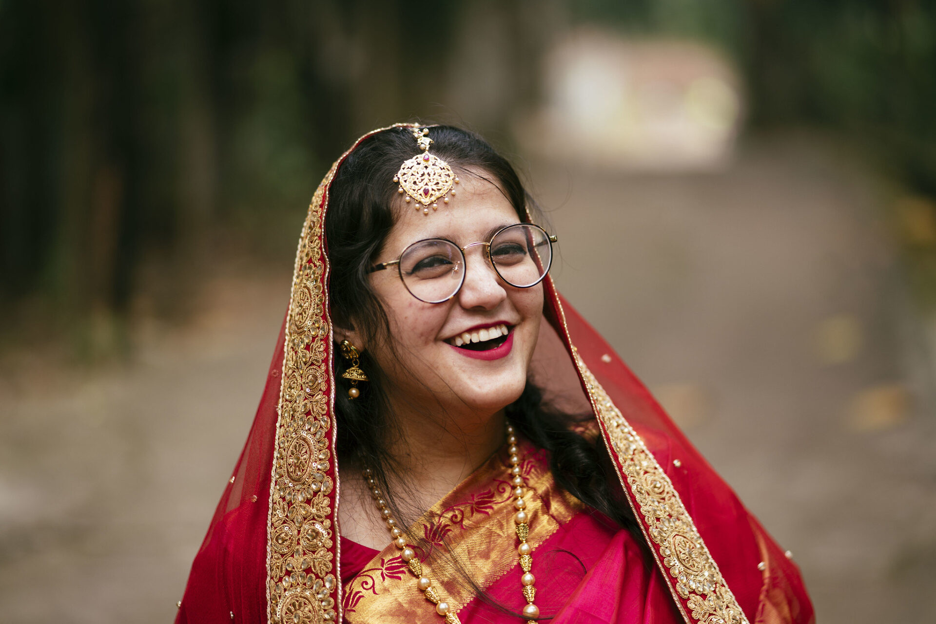 In Bangladesh, a bride wear smiles into the distance. She is wearing spectacles and a beautiful red sari.
