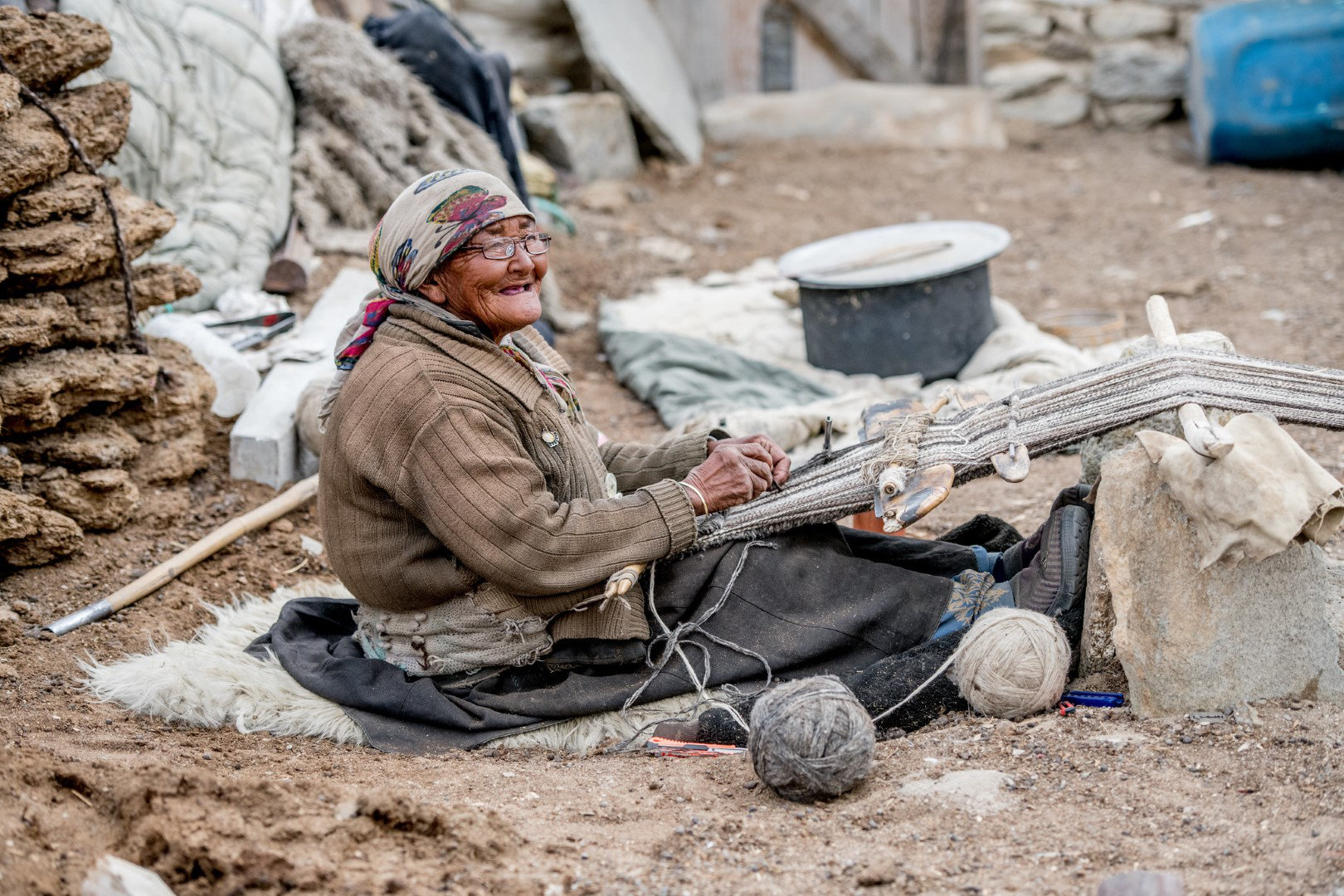 With the help of a new pair of glasses, a Ladakhi elder from the high altitude Changthang Plateau of Tibet, weaves a rug with wool from her hundreds of Pashmina goats. She smiles at the camera.