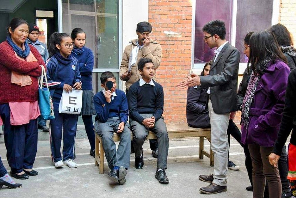 視光師在尼泊爾的學校眼科檢查計劃中，向學生和教師詳細解釋使用斯內倫視力表和針孔的視力評估程序。