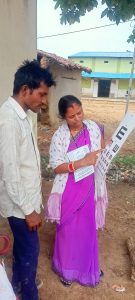 Female health worker wearing a purple sari stands beside a male patient wearing a white shirt, as she conducts a vision test