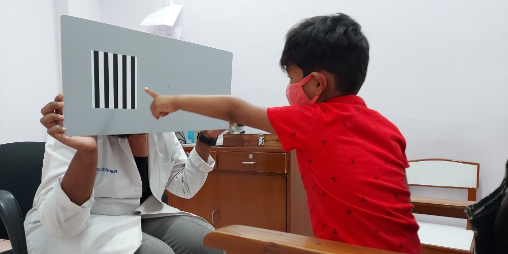 A doctor carrying out a TAC test in a boy child wearing a red tshirt and face mask