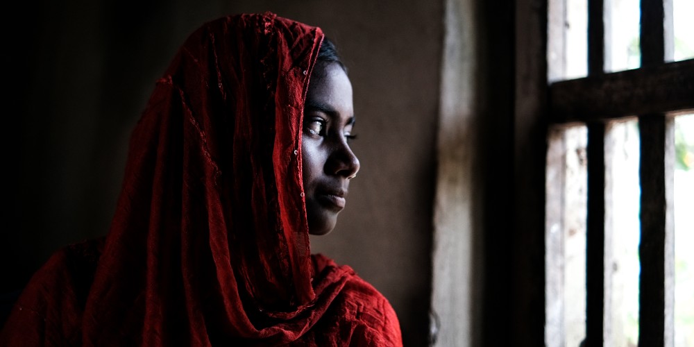 Girl with red headscarf looks out of a window