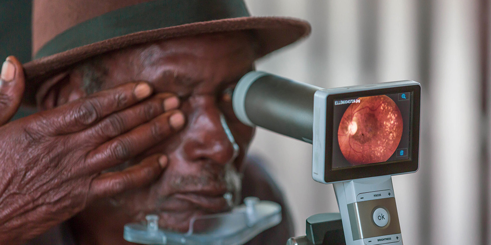 Un homme se fait examiner les yeux sur un appareil portable en Ouganda.