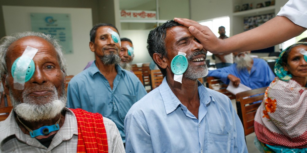 Quatre patients ayant subi une opération de la cataracte dans le cadre, l'accent est mis sur le patient dont le bonnet vert a été enlevé et qui sourit en posant la main sur son œil droit/Abir Abdullah