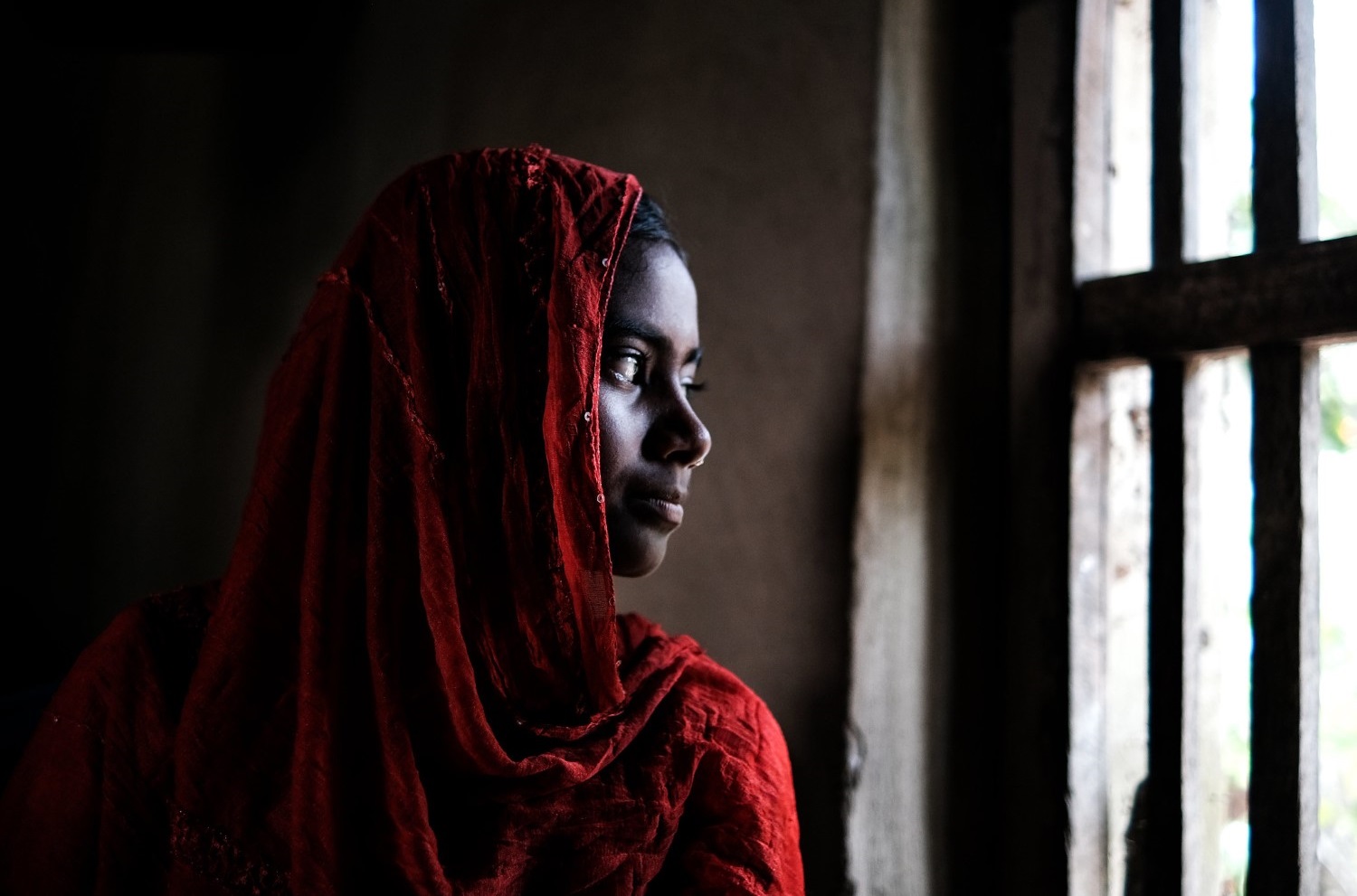 Woman looks out a window in a dark room in Bangladesh