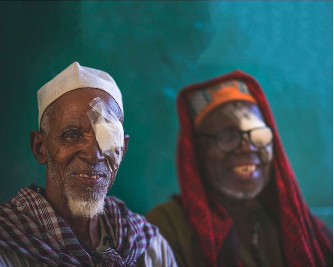 Two people with bandages over their eye smile at the camera.