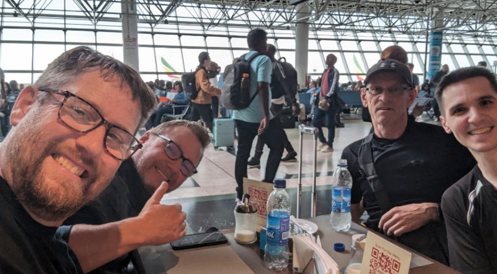 4 men at the airport smiling sat at a table waiting for food