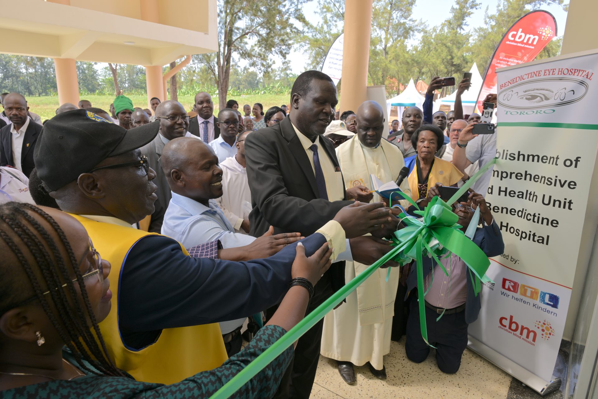 Cutting of the ribbon - from left to right: Jackie Kwesiga (CBM Country Director Uganda), Benon Katate (Lions Club International Uganda - yellow vest), Rev. Fidelis Ignatius Walwema (BEH Board of Governors) and Chief Guest Dr Alex Wasomoka (Assistant Commissioner in the Ministry of Health in Uganda representing the Minister of Health ). This photo was taken on the day of the comissioning of the Paediatric Eye Unit of the Benedictine Eye Hospital in Tororo, Uganda, on 20 February 2025. This new building and the equipment were made possible by donations from the ‘Stiftung Deutscher Lions’ and the ‘RTL - Wir helfen Kindern’ foundation through CBM (Christoffel Blindenmission Christian Blind Mission e.V.)