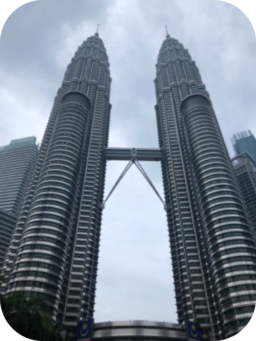 The Petronas Twin Towers in Kuala Lumpur, Malaysia, viewed from below against a cloudy sky.