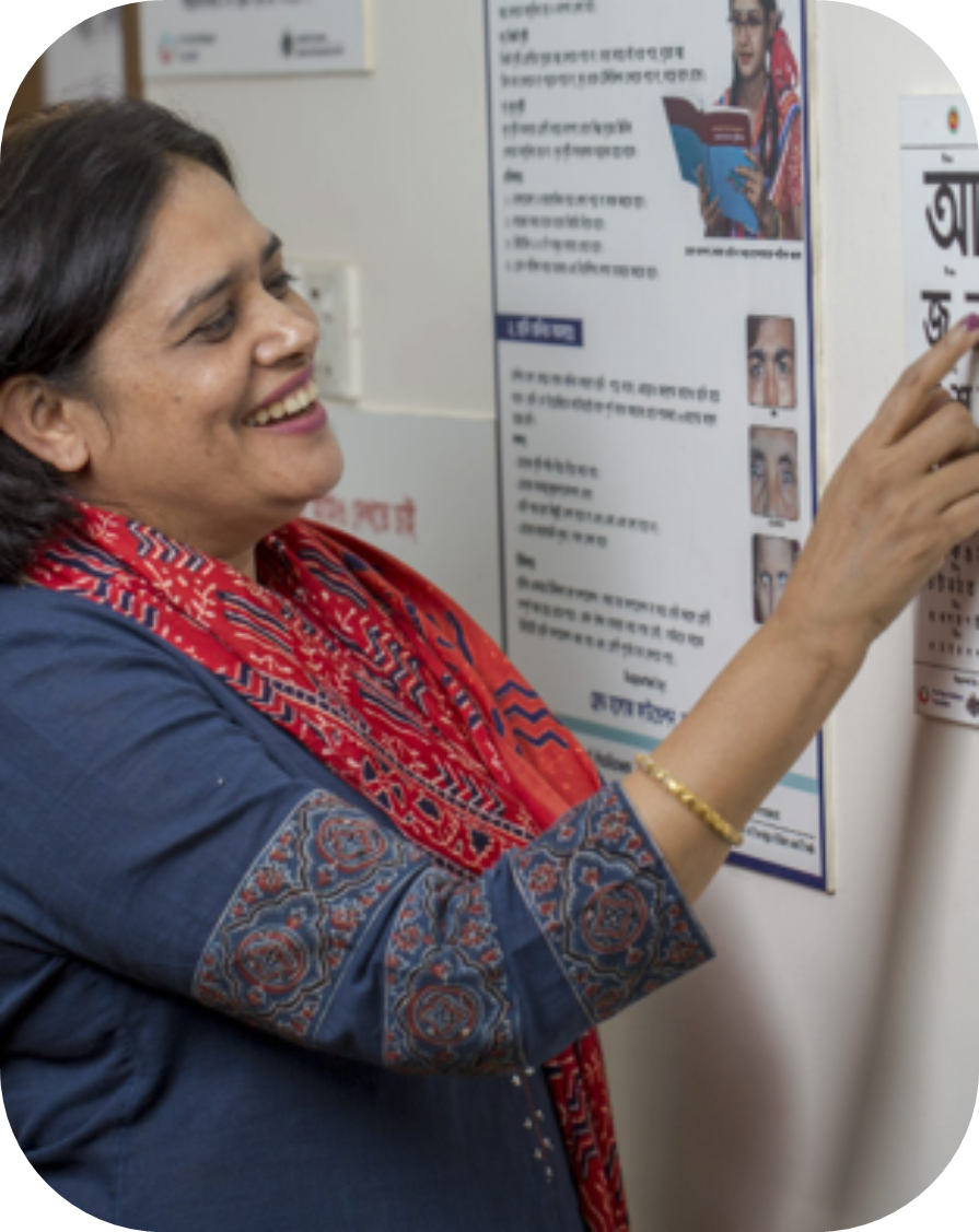 A woman in a red scarf smiles as she points to a vision chart on the wall.