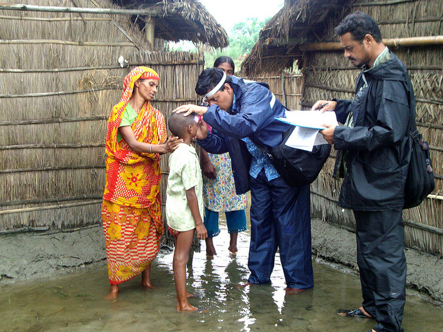 Eye test being conducted outside a straw hut in a water logged area in Bangladesh