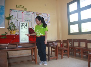 SCB staff member demonstrates reading an eye chart at Phu Tan Primary and Secondary School