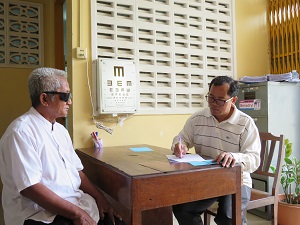 Pic courtesy: Seva cambodia. Old man sitting next to a vision chart.