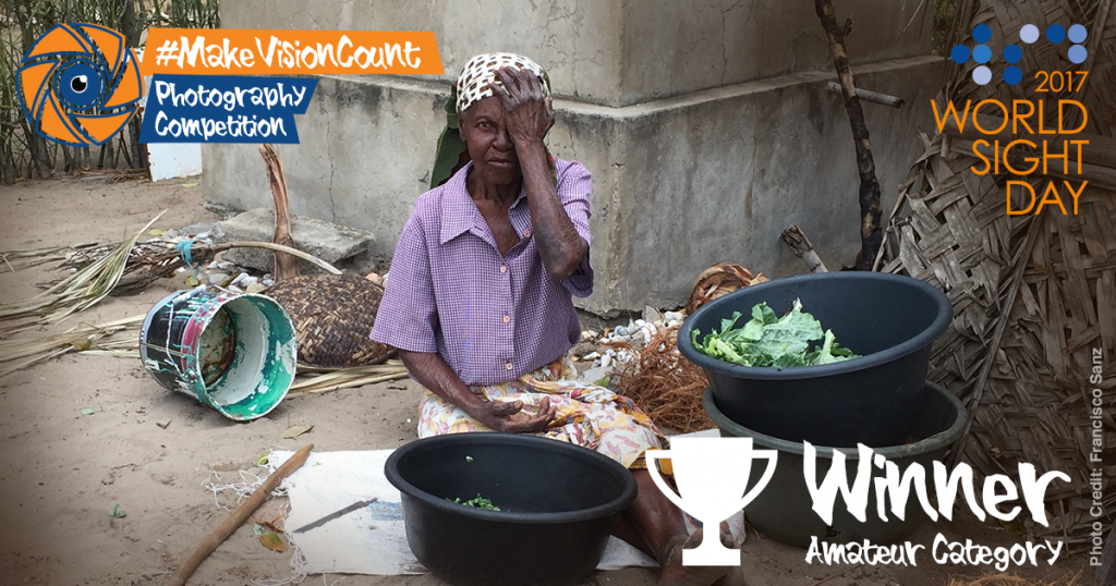 Woman sitting on the floor with baskets of vegetables. She is covering her left eye while taking an eye test.