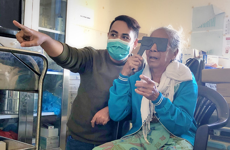 Man in mask providing a vision screening for an elderly woman